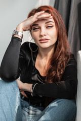 Fototapeta na wymiar Fashion portrait of pretty young woman with amazing blue eyes in black t-shirt and blue jeans sits and looks at the camera in room with sunlight