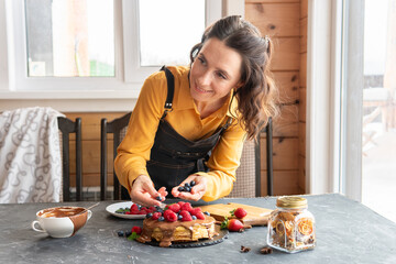 A woman is at the table with a cake of pancakes and berries for a holiday.