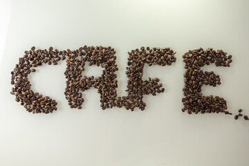 Das Wort Cafe geschrieben mit gold braunen gerösteten Kaffee Bohnen auf einer hellen Oberfläche