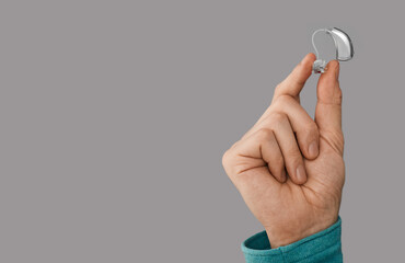 Hearing aid in male hand, close-up on gray background with space for text. Hearing solutions, BTE hearing aids