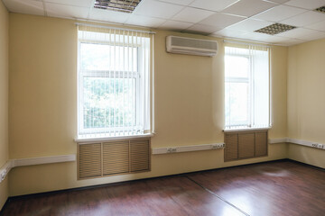 Not equipped empty office room with bright windows and air conditioner.