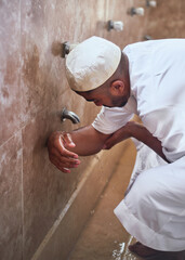 A young Muslim man performs wudu at a mosque during prayers by cleansing his arms with water