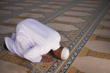 An overhead view of a Muslim man prostrate in prayer touching his forehead to the carpet in a mosque
