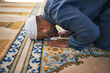 A close up of a Muslim man prostrate in prayer touching his forehead to the carpet in a mosque