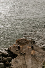 Relaxing scene at a holiday lounge deck by the sea overlooking blue waves and ocean, sun reflecting in water, blue sky and rocks in the background