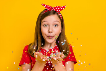 Photo of cute positive little teen woman blow send you confetti celebrate birthday isolated on yellow color background