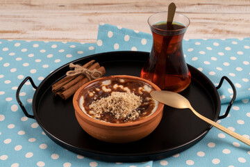 Baked rice pudding turkish milky dessert sutlac in earthenware casserole with walnuts served with a glass of tea and cinnamon sticks on a black metal tray
