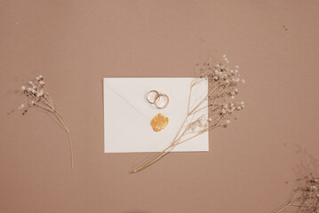 Wedding rings and invitations and craft envelopes on beigen background. Top view on paper cards, rings and dried flowers bouquet, copy space. Memmorable date organization concept