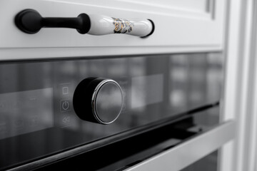 Kitchen furniture with built-in electric oven, original ceramic handle on white cabinet, selective...