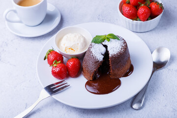 Lava cake - chocolate fondant cake with vanilla ice cream, strawberries, mint and coffee. Traditional French pastries. Close-up.