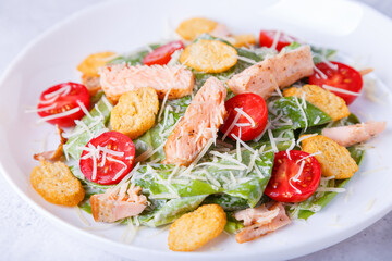 Caesar salad with red fish (salmon, trout), cherry tomatoes, croutons, parmesan cheese and romaine. Traditional American dish. Close-up, selective focus.