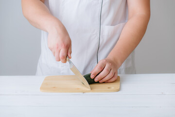 the hands of the cook cut the cucumber on a wooden board, on a white background