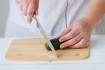 the hands of the cook cut the cucumber on a wooden board, on a white background
