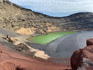 Volcanic green lake in volcanic crater with black and bricky sand an rocks