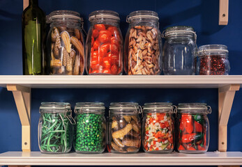 Glass jars with pickled and salted vegetables on a shelf in a kitchen interior. Homemade food.