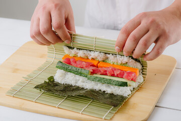 the chef cook prepares sushi and wraps a letter to the nori in the roll, on white background