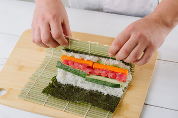 the chef cook prepares sushi and wraps a letter to the nori in the roll, on white background