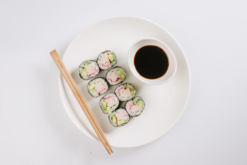 Sushi with chopsticks on a white plate. Sushi roll japanese food in restaurant isolated on white background. Fresh hosomaki pieces with rice and nori.