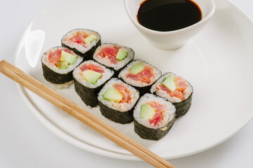 Sushi with chopsticks on a white plate. Sushi roll japanese food in restaurant isolated on white background. Fresh hosomaki pieces with rice and nori.