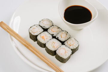 Sushi with chopsticks on a white plate. Sushi roll japanese food in restaurant isolated on white background. Fresh hosomaki pieces with rice and nori.