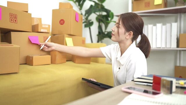 good looking asian woman Checking stock, preparing to pack items to be sent to customers. A lot with tabrets, concepts, online business online products work from home sme