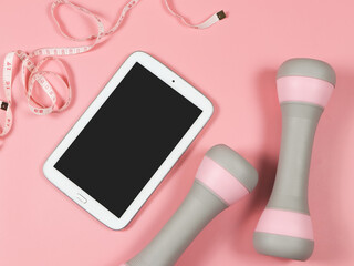 flat lay of blank black screen computer tablet, pink dumbbells and measuring tape on pink...