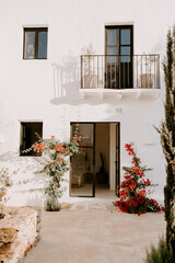 A serene Ibiza-style patio with a white stucco wall, sheer curtains, a woven rattan chair, and vibrant bougainvillea, creating a peaceful Mediterranean retreat bathed in natural sunlight