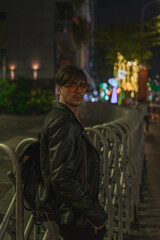 Portrait of young stylish brunet caucasian man in black leather jacket and yellow sunglasses Standing near the iron fence. High quality photo