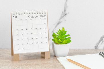October 2022 desk calendar with plant on wooden table.