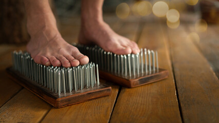 Male bare feet stand on a Sadhu boards with sharp nails on wooden floor indoor, close up, selected focus. - obrazy, fototapety, plakaty