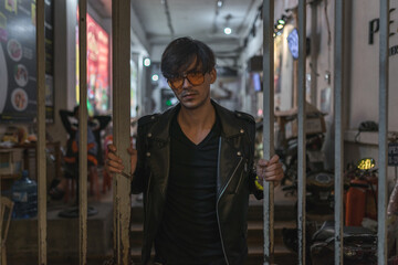 Portrait of young stylish brunet caucasian man in black leather jacket and yellow sunglasses Standing near the iron fence. High quality photo