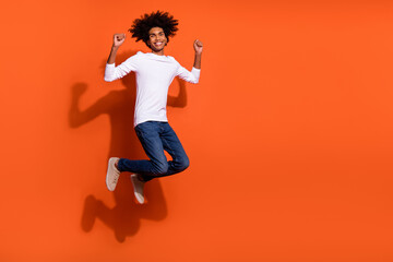 Fototapeta na wymiar Photo of lucky charming guy wear white shirt jumping high rising fists empty space isolated orange color background