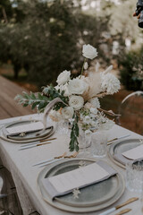 Elegant outdoor destination wedding table setup with white linens, floral centerpieces, transparent chairs, and string lights, creating a romantic and intimate atmosphere for a special celebration