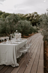 Elegant outdoor destination wedding table setup with white linens, floral centerpieces, transparent chairs, and string lights, creating a romantic and intimate atmosphere for a special celebration