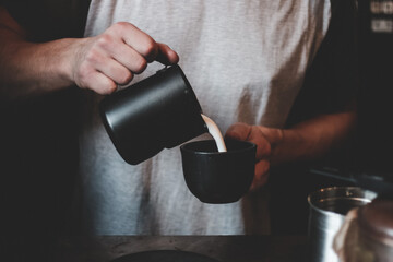 Male barista pouring milk into coffee cup