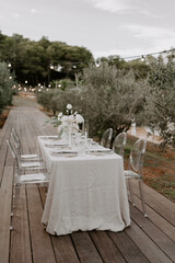 Elegant outdoor destination wedding table setup with white linens, floral centerpieces, transparent chairs, and string lights, creating a romantic and intimate atmosphere for a special celebration