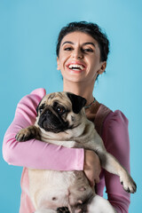 laughing woman with funny pug in hands looking at camera isolated on blue