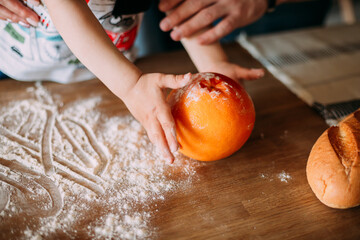 children's hands with orange and flour on the kitchen table