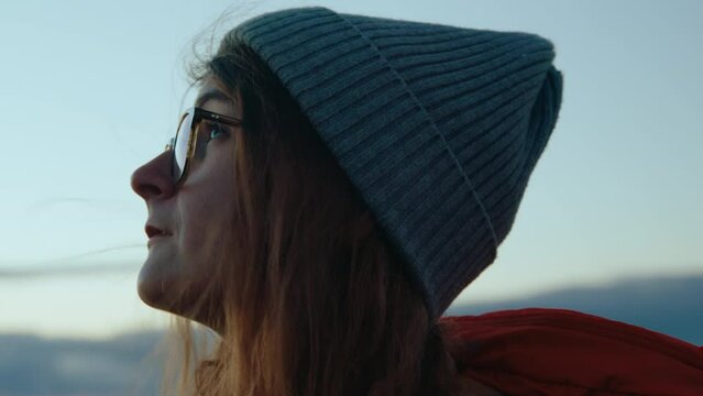 Authentic and cinematic portrait of real young woman stand on mountain top and look at sky, enjoy nature and quiet. Concept mindfulness and peace, new generation of conscious and responsible consumers