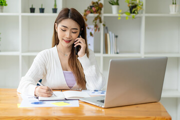 A young Asian woman accountant sits at her desk with her laptop and calculates financial graphs showing investment results. Plan a successful business growth process in the office.