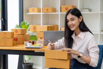 Obraz na płótnie Canvas Starting a Small Business, SME, Independent Entrepreneur Asian woman working at home with cardboard boxes, smartphones, laptops, online, marketing, packaging, transportation, SME, e-commerce concept.