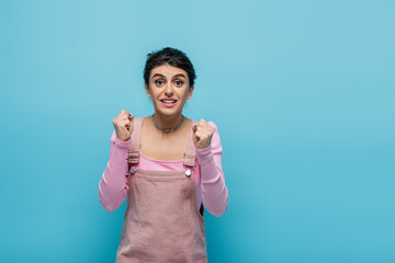 hopeful and positive woman holding clenched fists for luck isolated on blue