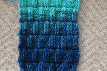 The canvas is knitted from melange yarn with knitting needles. The knit and purl stitches alternate in the pattern. Knitting is a hobby for many women.