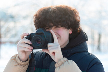 A boy with dark curly long hair takes a picture with a DSLR camera. Wonderful winter photo shoot outdoors