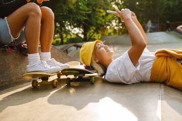 Asian girl laughing and using mobile phone while lying at skate park