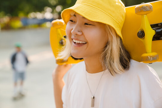 Asian Girl Wearing Hat Holding Skateboard While Laughing