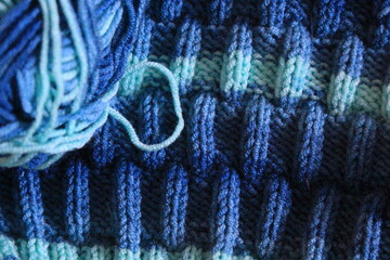 The canvas is knitted from melange yarn with knitting needles. The knit and purl stitches alternate in the pattern. Knitting is a hobby for many women.