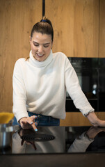 Pretty girl setting up the ceramic hob in her kitchen at home before cooking.