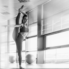 Beautiful young sportive woman doing vertical split standing on one leg, monochrome image aspect...
