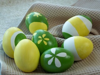Easter eggs painted with yellow and green paint depicting flowers and stripes lie on a kitchen towel. Preparation for Easter, decor